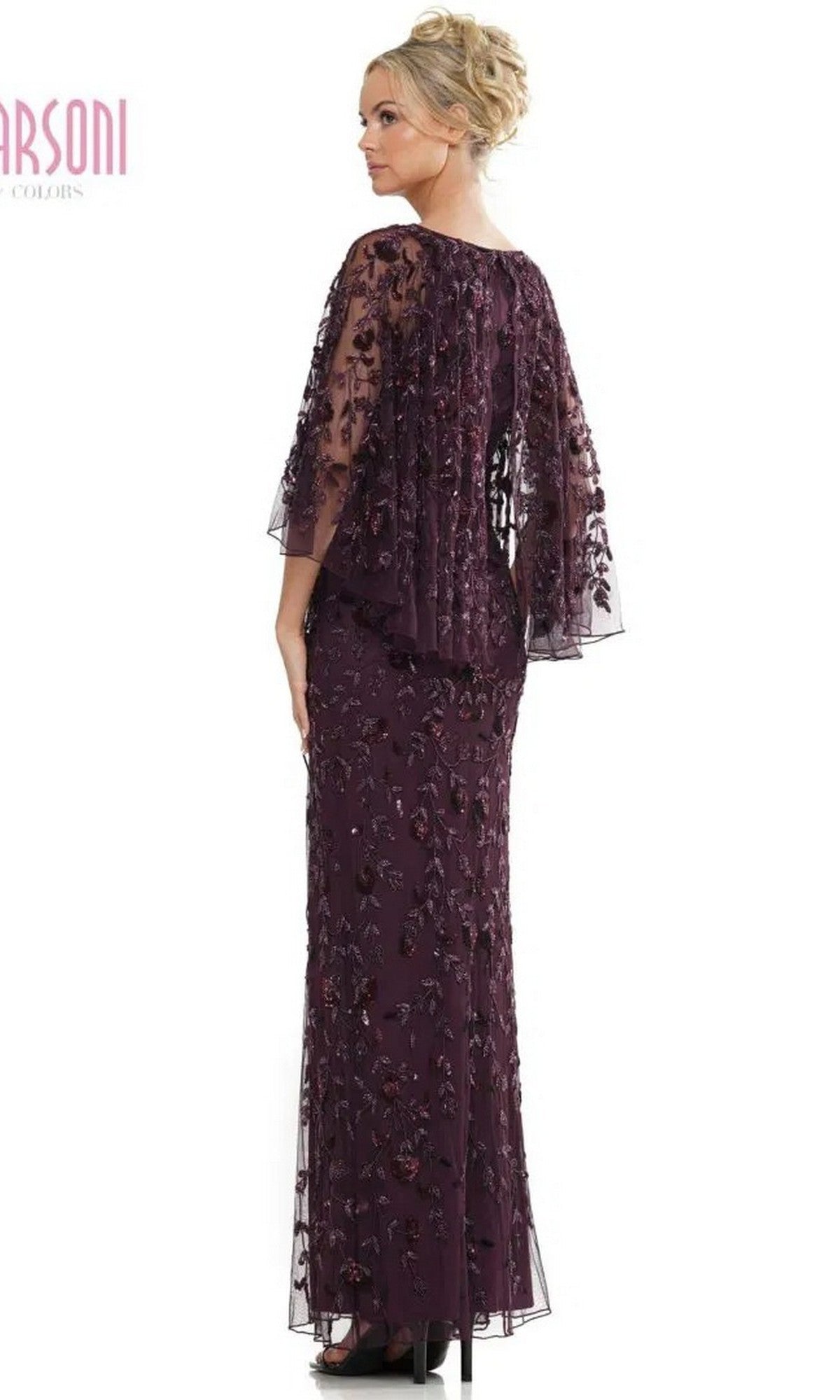 A woman stands facing away, wearing the Marsoni MV1282 long formal dress in dark purple, featuring floral embroidery, beaded leaf appliques, and a sheer capelet.
